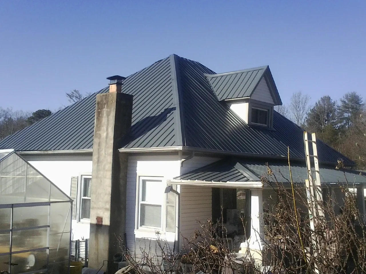 Dark blue standing seam metal roof on a white farmhouse with dormer — Slate & Tile Roof Repair by Roofing Brothers in Primghar