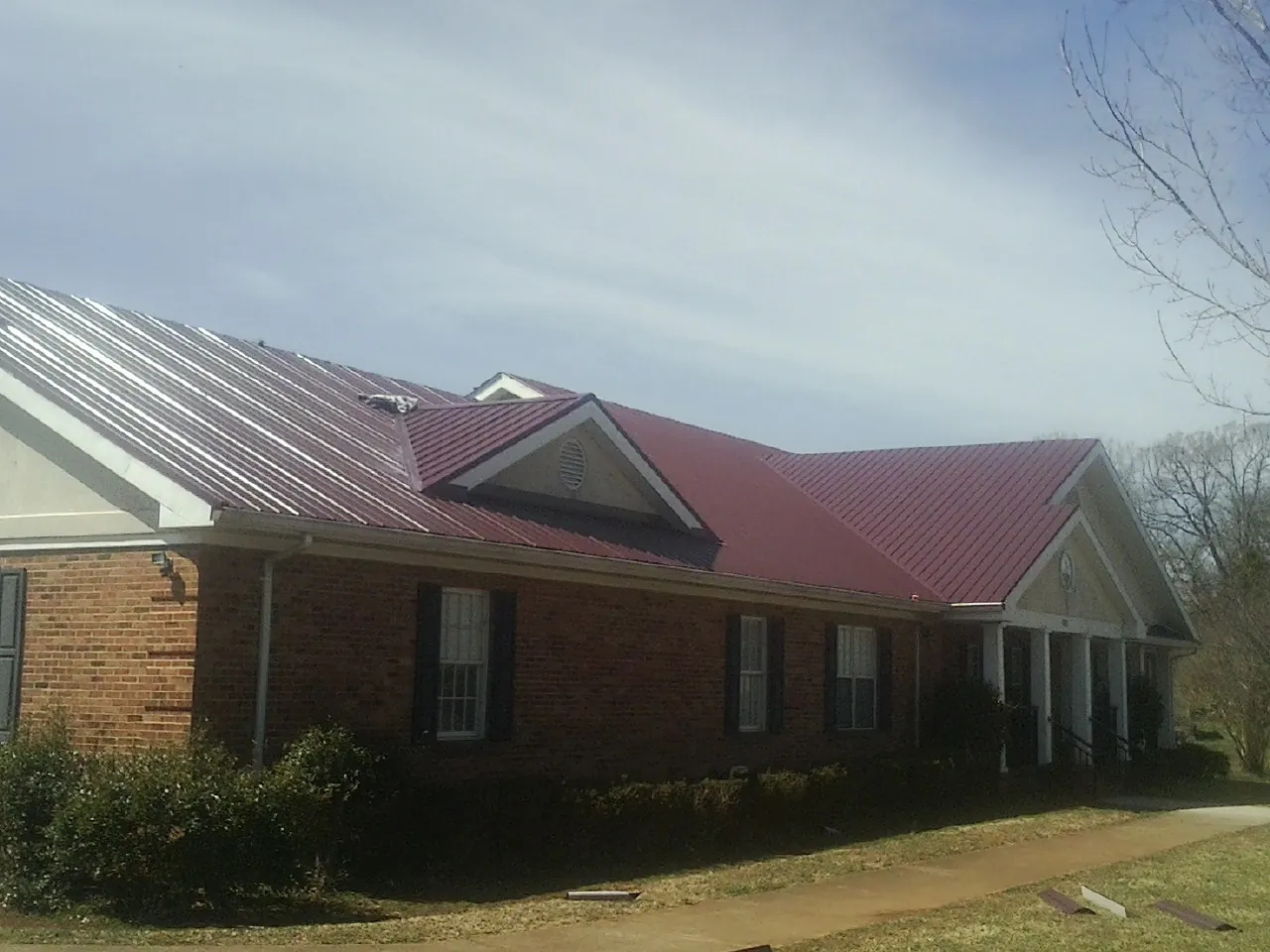 Red metal roof with gabled entries on a long brick building, from a Hail Damage Roof Repair job in Primghar