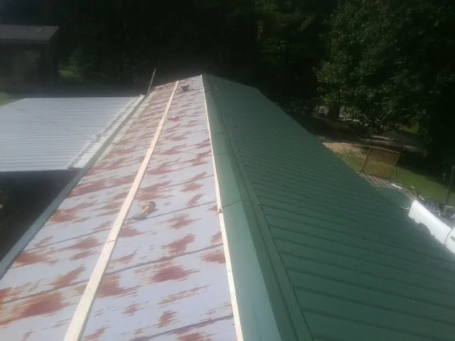 Old rusted panels beside newly installed green metal roofing — Wind Damage Roof Repair by Roofing Brothers in Primghar