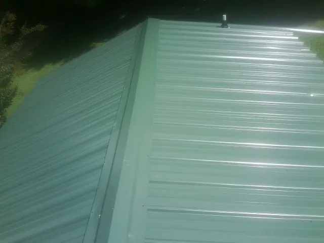 New green metal panels meeting at the ridge of a roof — Flat Roof Repair work by our crew in Primghar