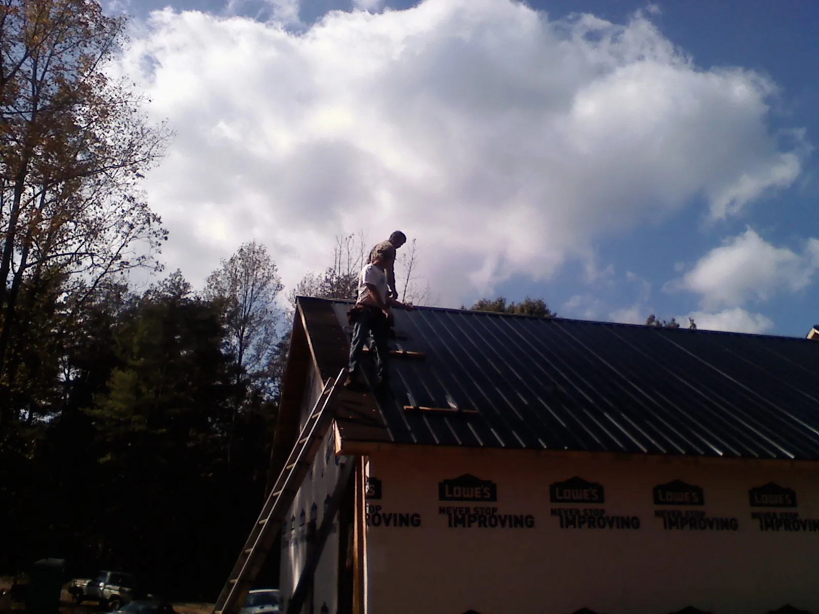Roofer fastening dark metal panels high against a cloudy sky, from a Roof Inspection job in Primghar