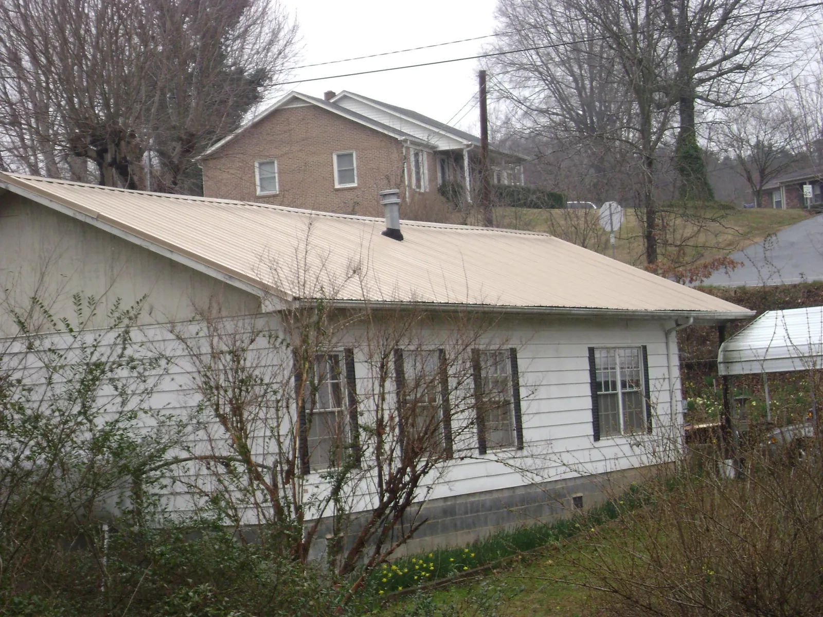 Tan metal roof on a white sided house set into a hillside — Commercial Roofing by Roofing Brothers in Primghar